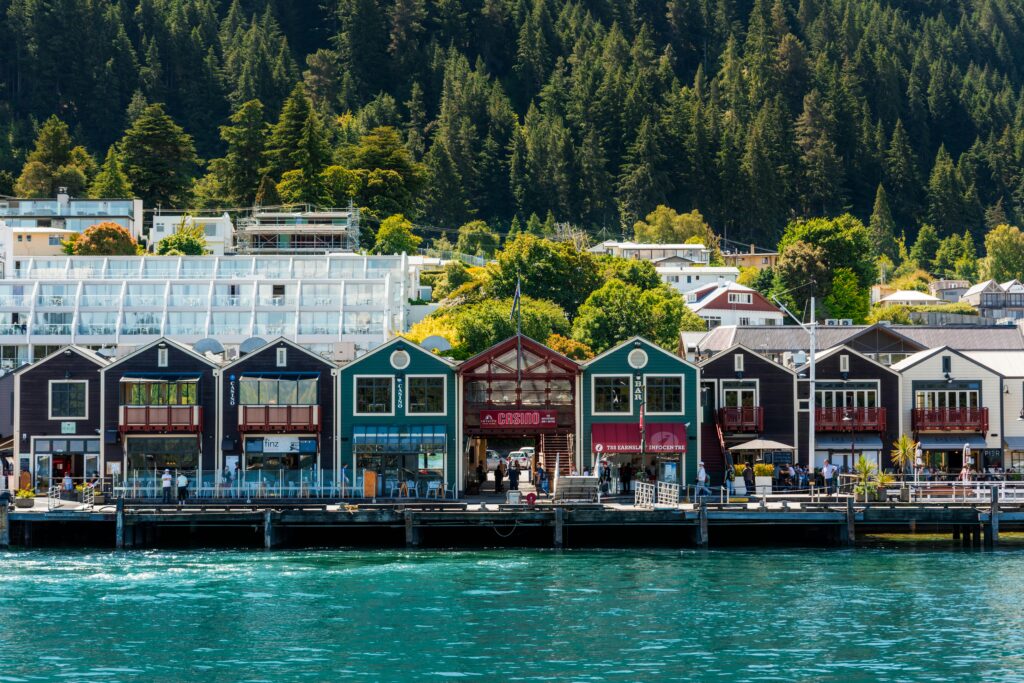 Colorful waterfront buildings in Queenstown with mountainous backdrop and vibrant greenery.